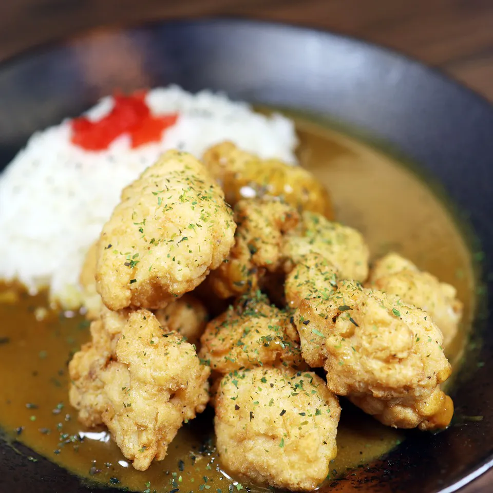A dark bowl of Japanese curry featuring a heap of golden-brown fried chicken karaage pieces sprinkled with dried parsley, served next to a mound of white rice topped with red pickled ginger at Unique Cafe, a Japanese restaurant in Ontario