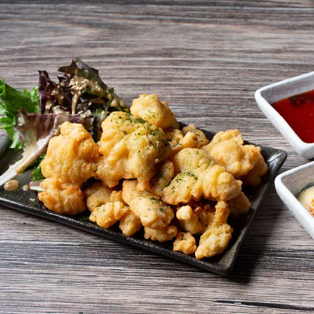 A black rectangular plate piled with crispy, golden-fried chicken karaage pieces garnished with parsley, served with a side of mixed salad greens and two small dipping sauce dishes at Unique Cafe, a Japanese restaurant in Ontario