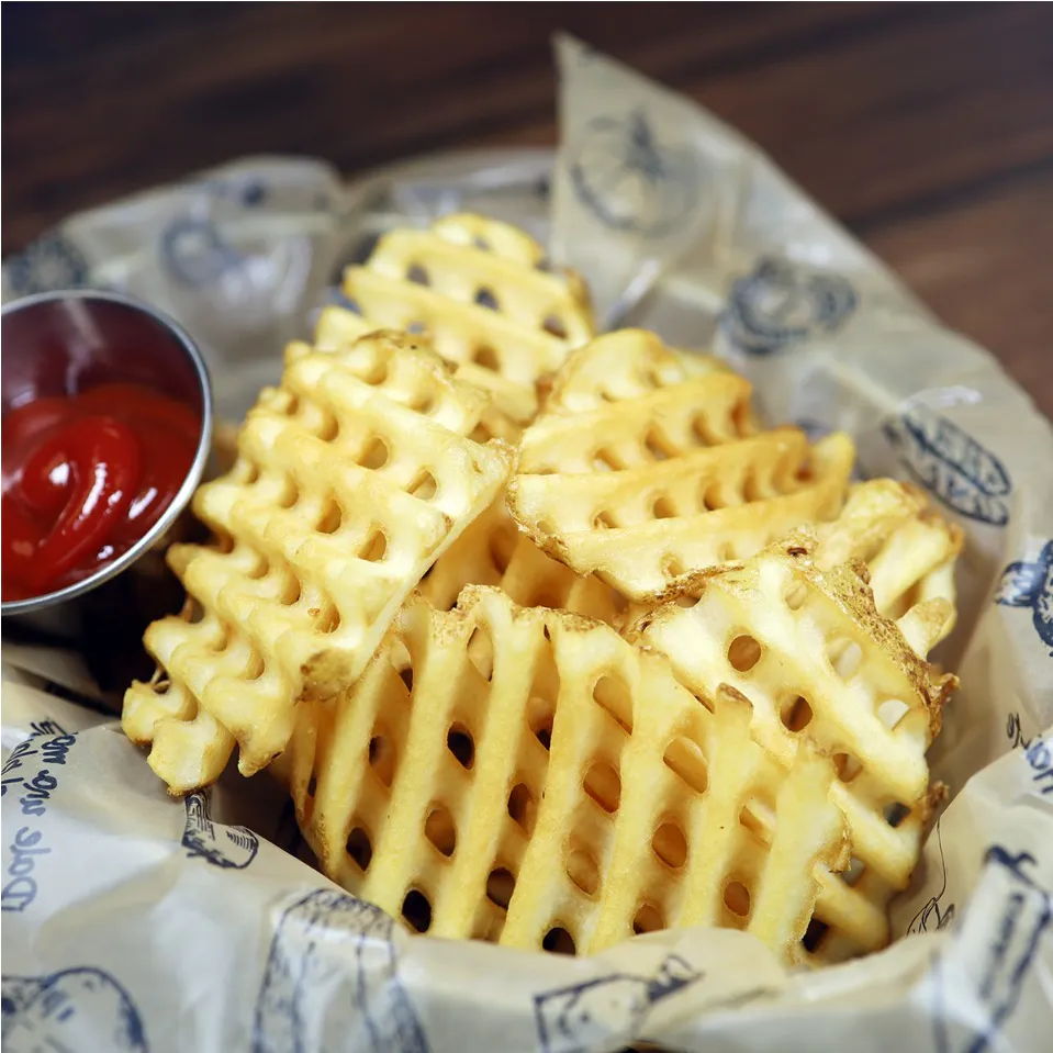 A basket lined with patterned parchment paper holding a pile of golden, crispy waffle-cut french fries, served with a small metal cup of red tomato ketchup at Unique Cafe, a Japanese restaurant in Ontario